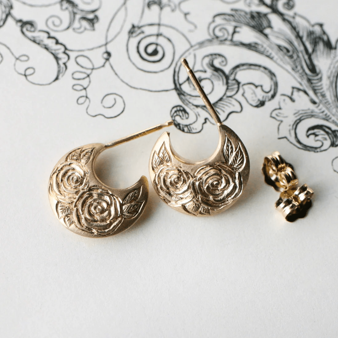 14k gold Beloved Rose earrings by Blue Blue Driver displayed on a decorative background with earring backs.