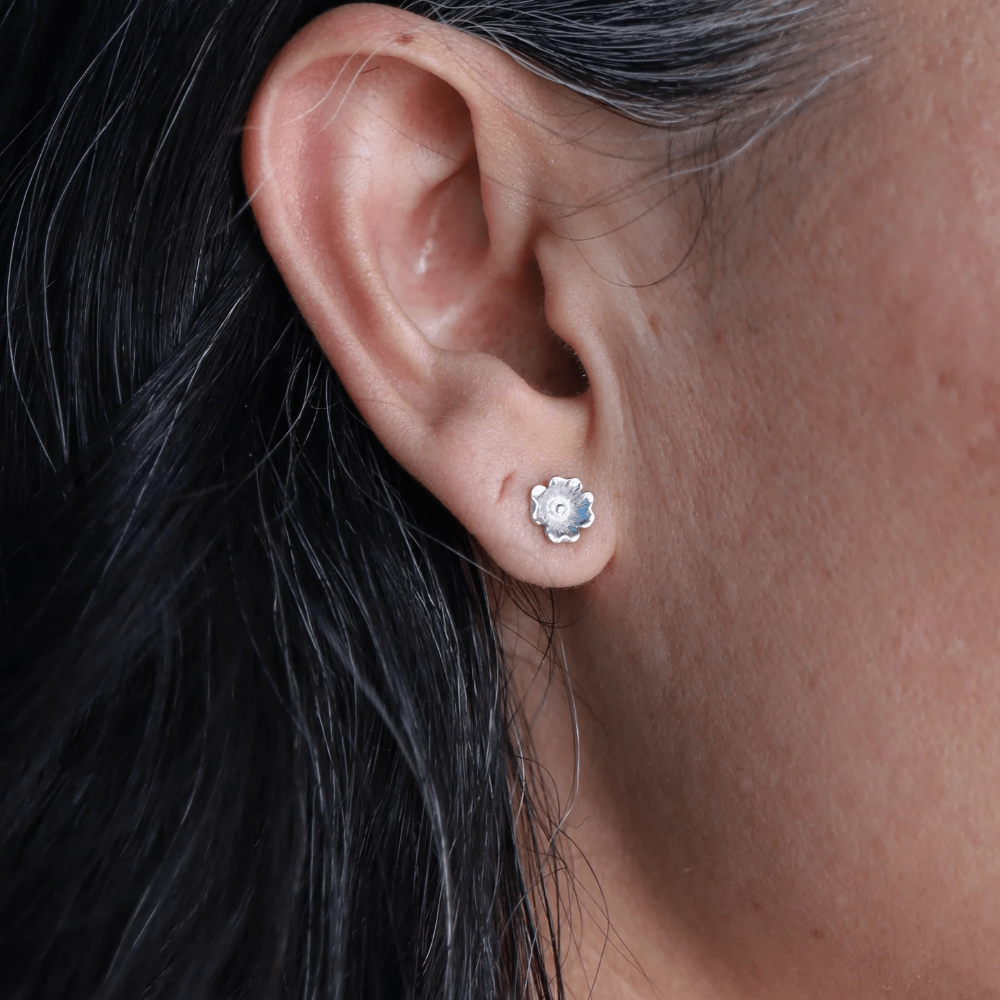 Silver dogwood flower stud earring worn on the ear.
