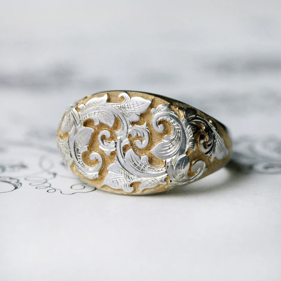 Gold and silver East-West Acanthus Signet Ring with ornate hand-engraved scrollwork on a light background.