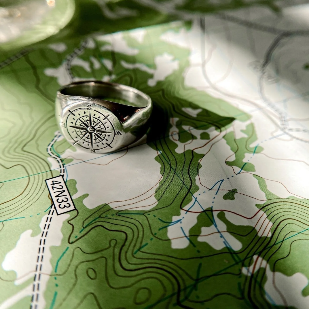 Sterling silver compass ring photographed on a hand over a topographic map.
