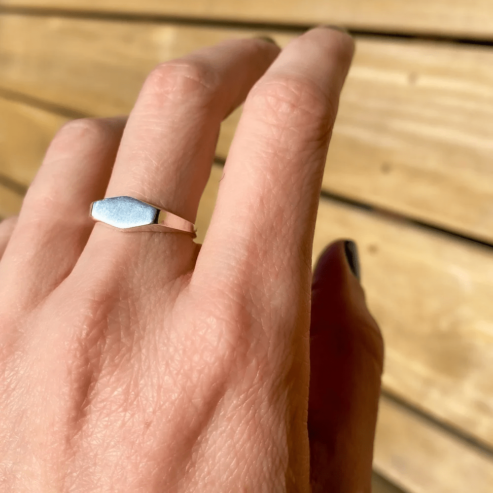 Sterling silver Crest Signet Ring worn on hand in natural sunlight with wooden background.