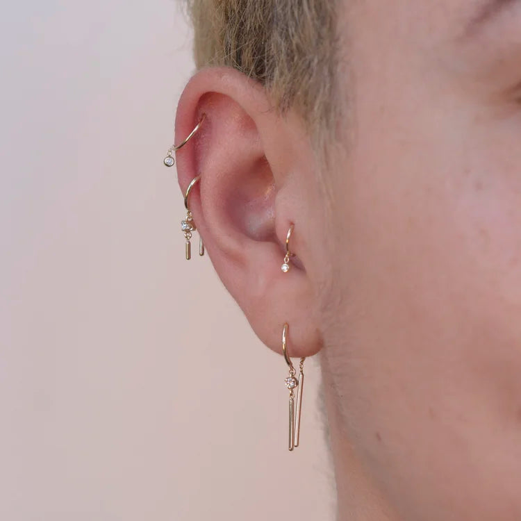 14k gold diamond droplet huggie earring worn on ear in a cartilage stack.