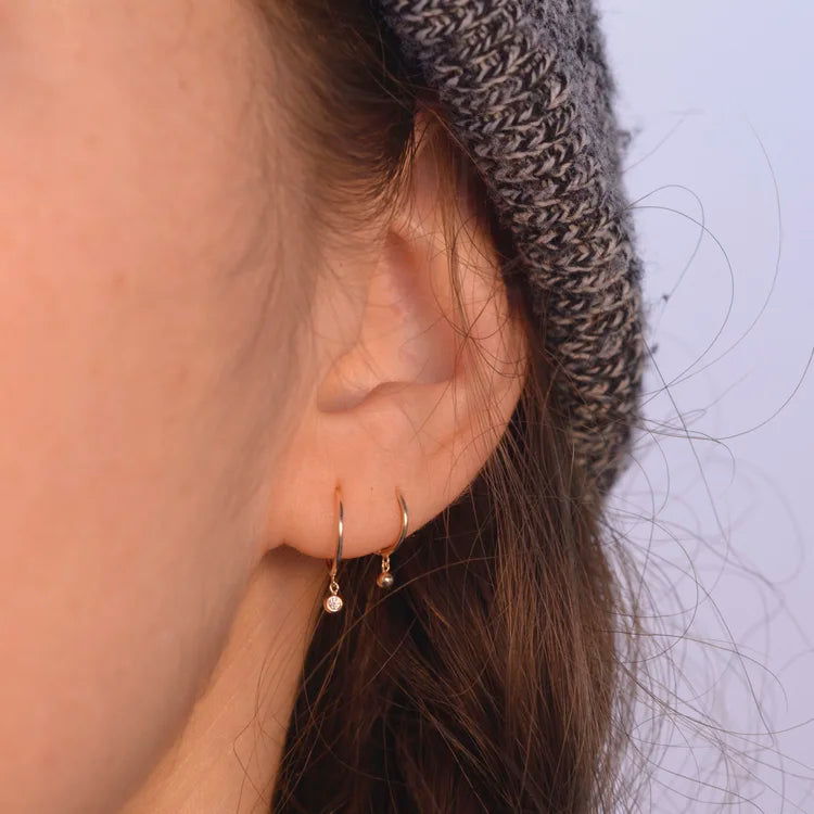 Close-up of model wearing a 14k gold diamond droplet huggie earring.