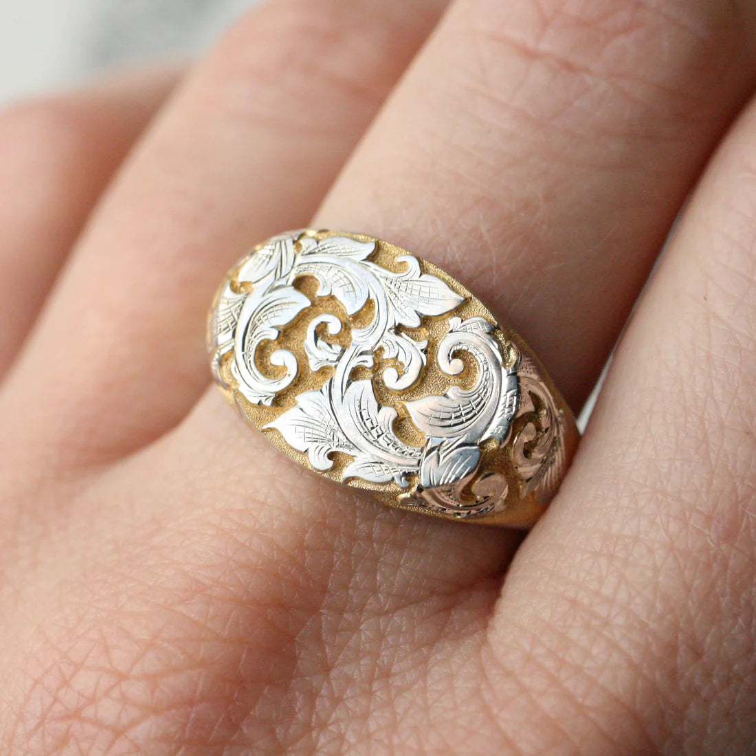Close-up of the East-West Acanthus Signet Ring in 14k yellow gold & silver background, shown worn on a hand.