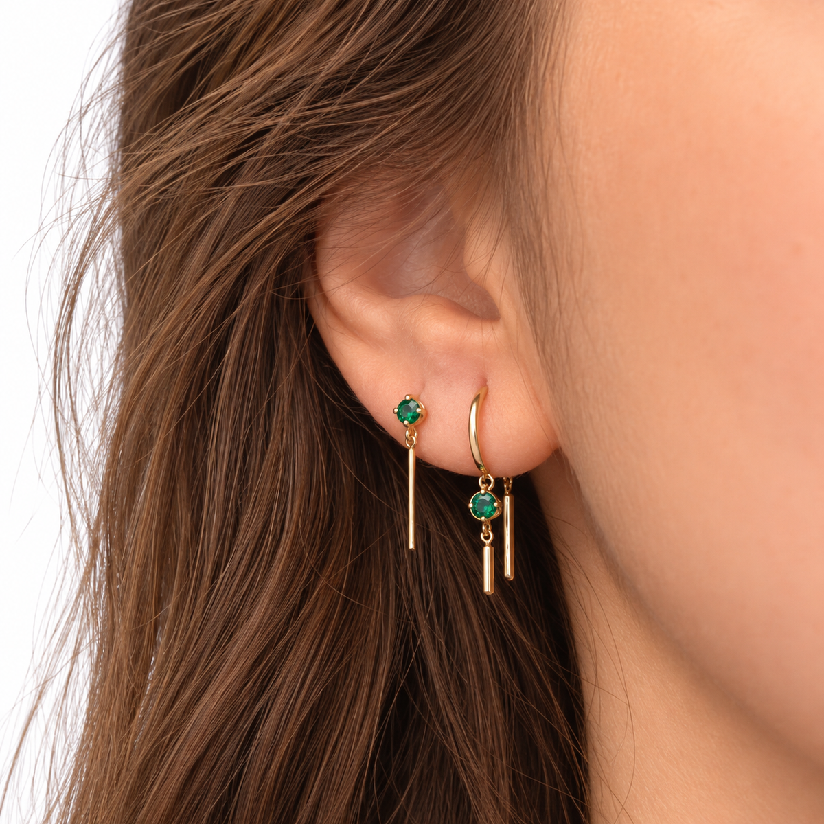 Close-up of a model wearing a petite emerald chime earring in 14k yellow gold, styled with other delicate gold earrings.