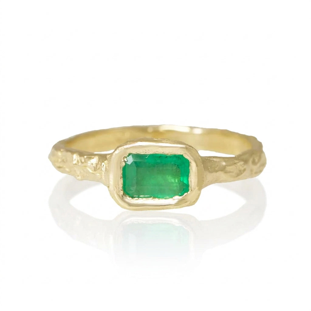 Front view of the Emerald Metamorphic Ring III by Alexis Pavlantos, featuring a 0.43 carat emerald-cut green emerald in a sculptural 14k yellow gold setting with hand-carved rock texture.