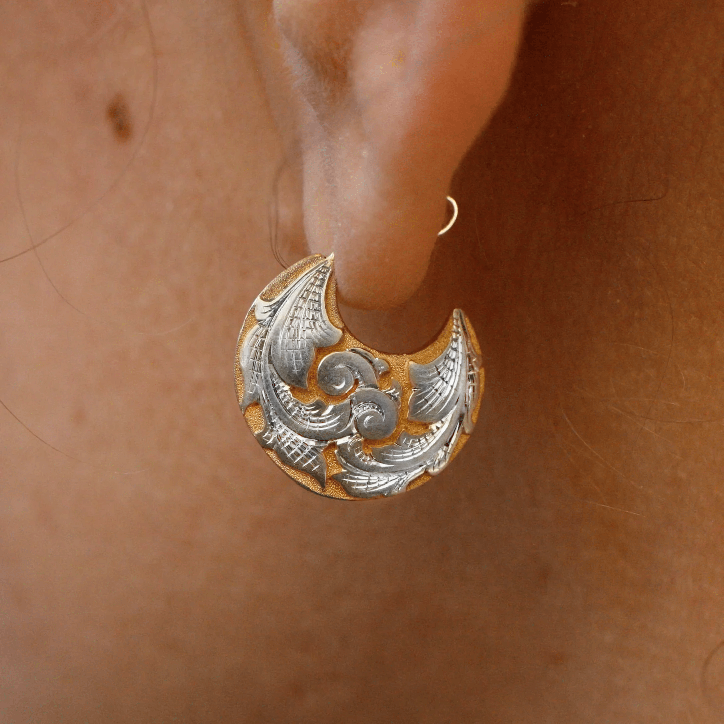 Sterling silver engraved crescent earring worn on ear – detailed scroll motif.