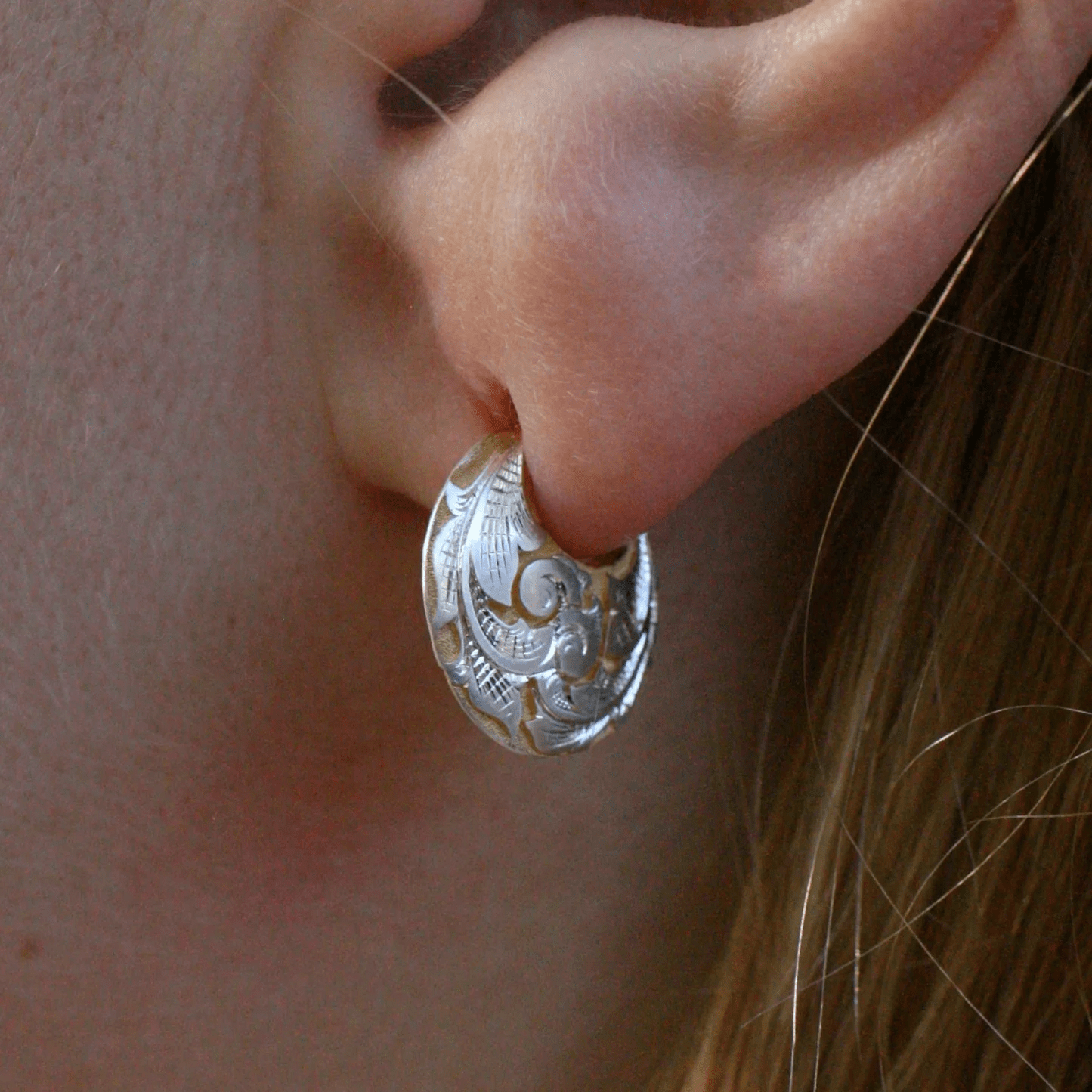 Two-tone engraved crescent earring worn on ear – hand-engraved scroll and leaf design.