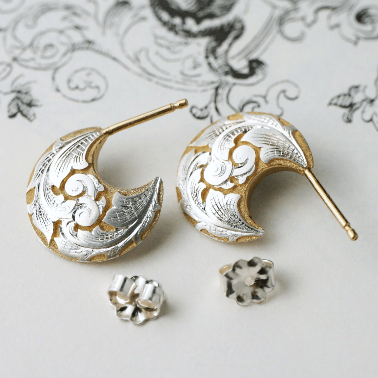 Pair of two-tone engraved crescent earrings on decorative background with earring backs.