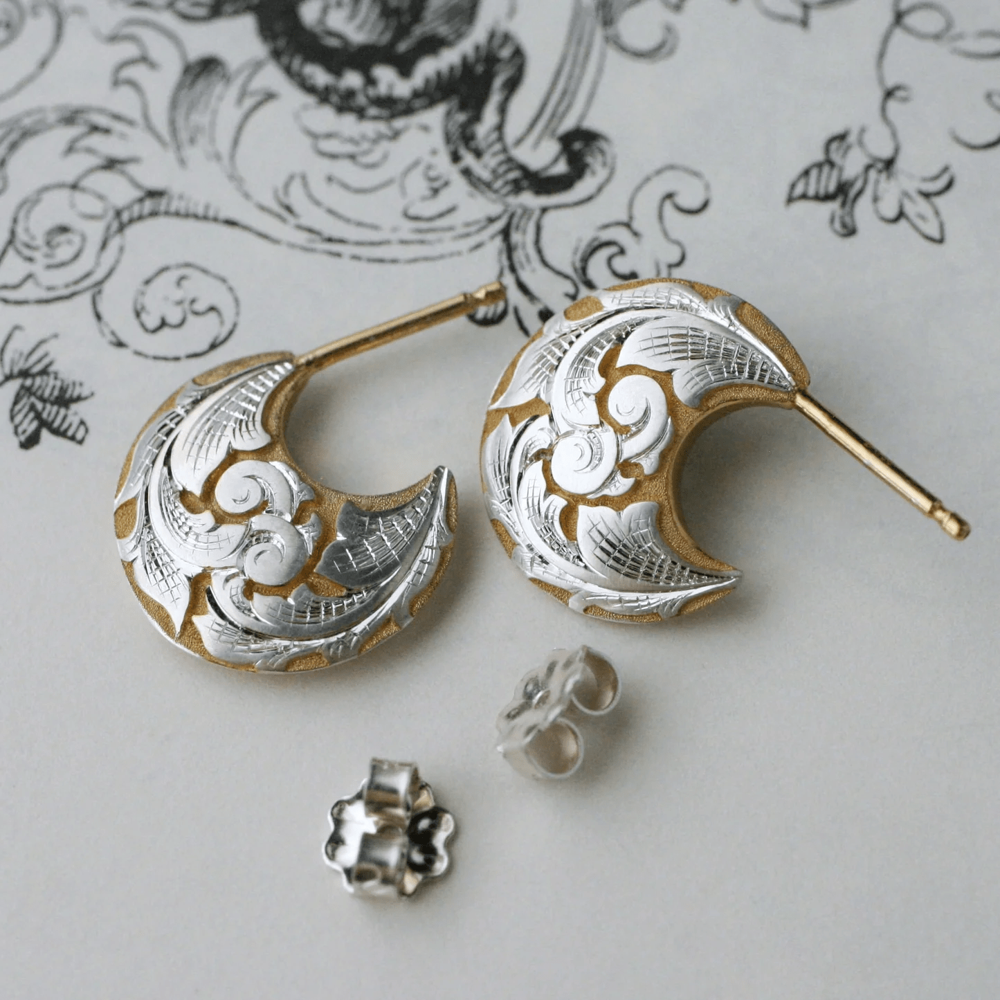 Two-tone crescent earrings displayed with backs – hand-engraved scroll and leaf details.
