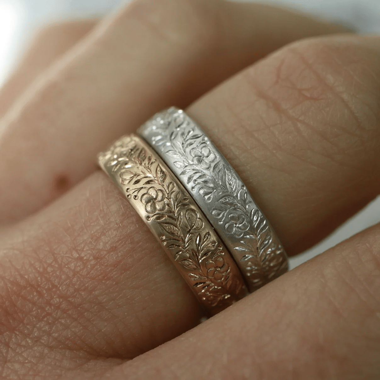 Gold and white engraved floral band rings worn together on a hand.
