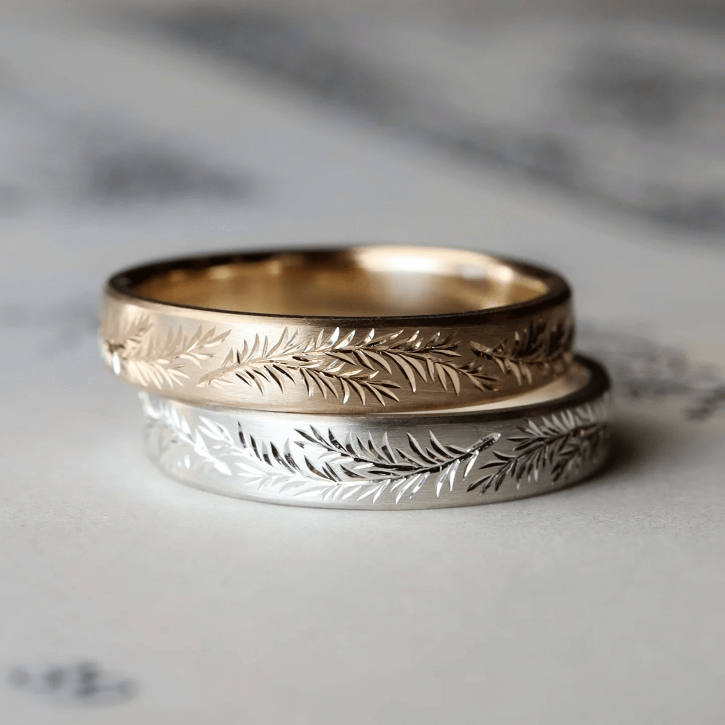 Gold and silver engraved rosemary bands stacked together on decorative background.