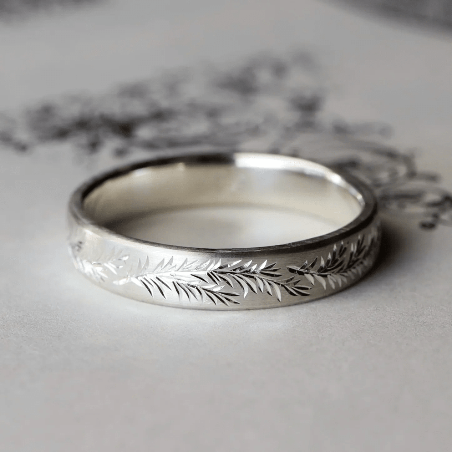 Sterling silver engraved rosemary band ring on decorative background.