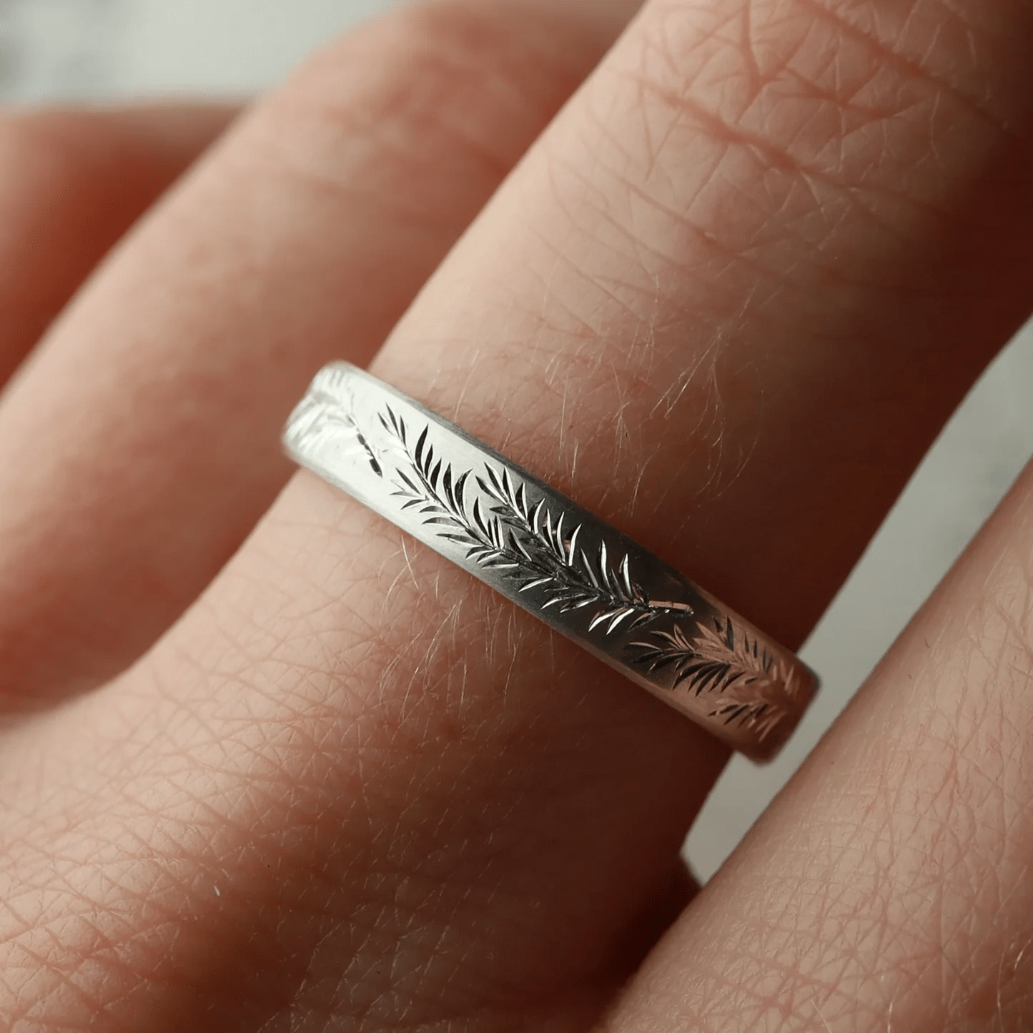 Silver rosemary engraved band worn on hand – delicate leaf pattern.