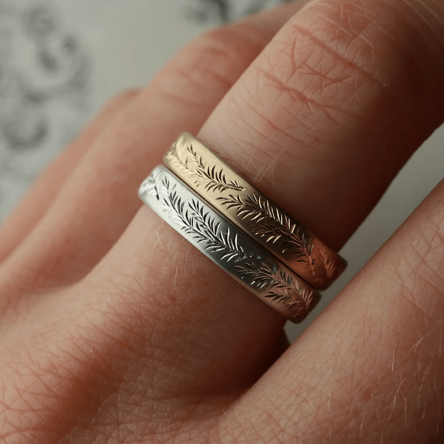 Stack of engraved rosemary band rings in silver and gold worn on finger.