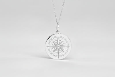 Round silver-tone pendant necklace with a detailed engraved compass-style design, displayed against a light background.