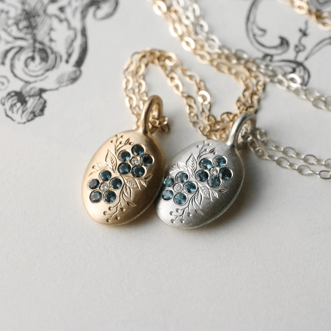 Gold and sterling silver forget-me-not pendants shown together, each set with London blue topaz stones.