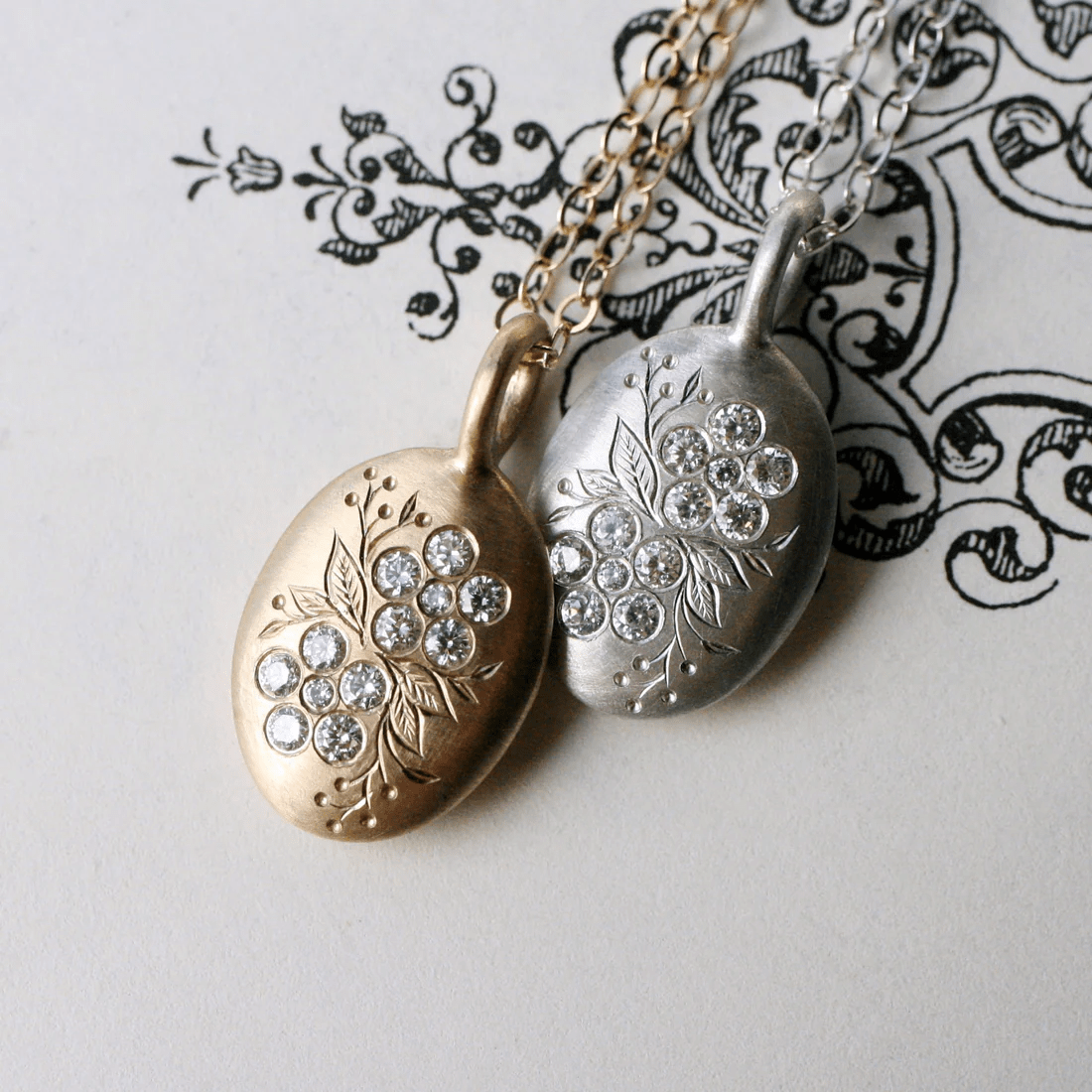 Side-by-side display of gold and silver forget-me-not pendants, both featuring hand-set diamonds.