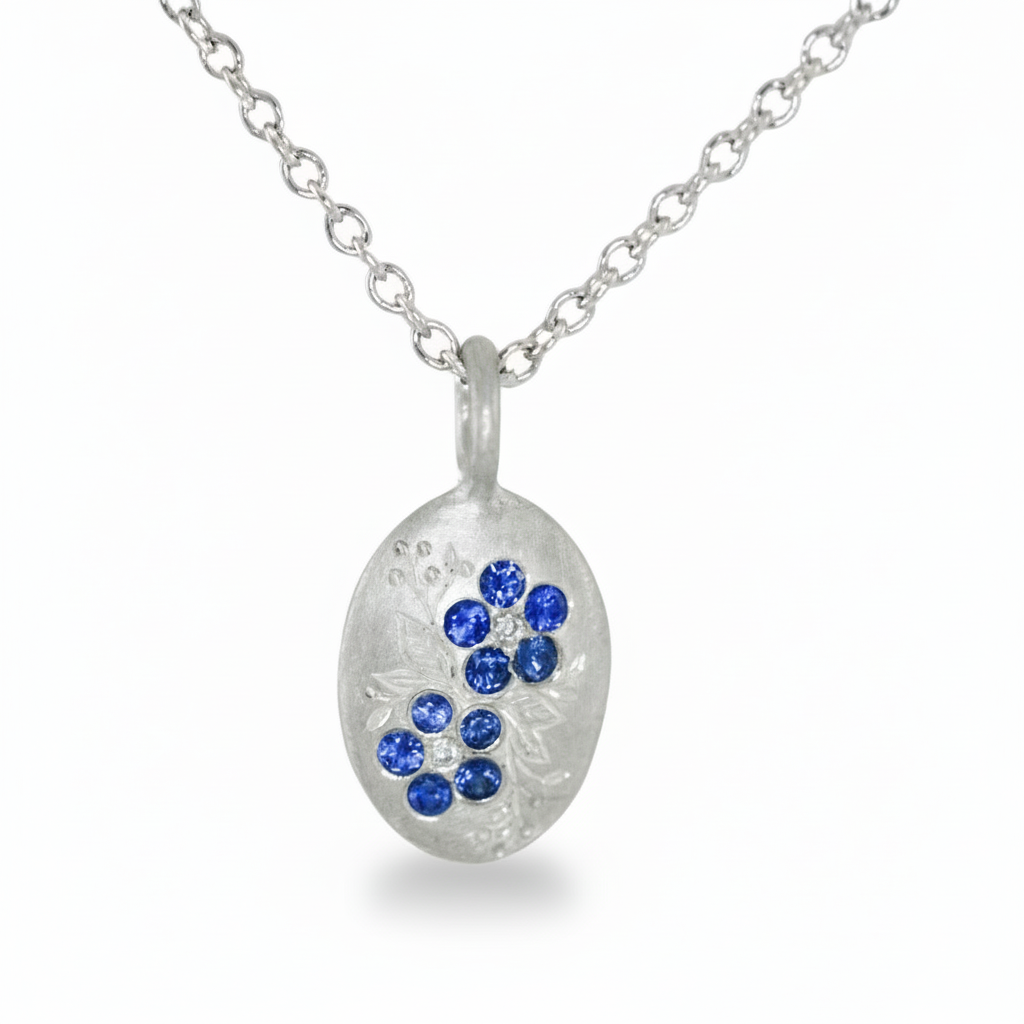 Silver forget-me-not pendant with London blue topaz stones on a white background.