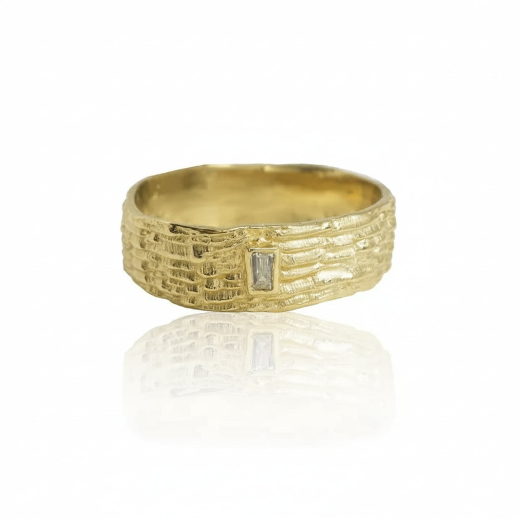 Front view of the Sparkle Fractured Ring by Alexis Pavlantos, featuring a wide 14k yellow gold band with hand-carved geological textures and a vertically set baguette diamond.