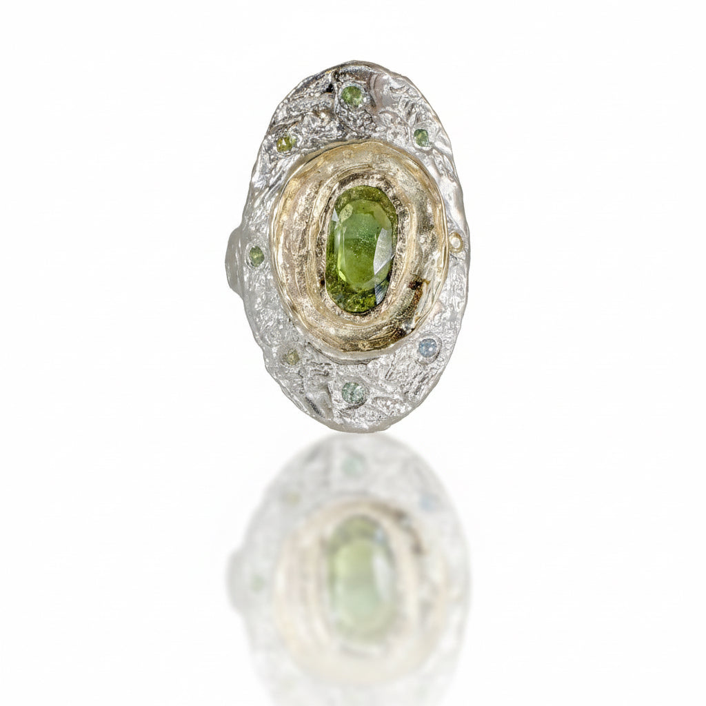 One-of-a-kind Fragmented Green Sapphire Ring II by Alexis Pavlantos, featuring a 1.30ct rose-cut green sapphire in recycled 14k yellow gold, surrounded by six accent sapphires on a textured sterling silver band.