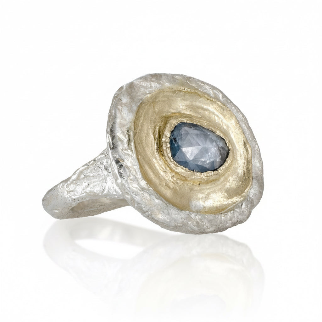Angled view of the Fragmented Ring III showing its pear-shaped blue sapphire, layered 14k yellow gold setting, textured sterling silver band, and sculptural mixed-metal design.