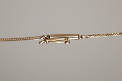 Close-up of a delicate gold-tone jewelry chain with a clasp and connecting links against a neutral gray background.