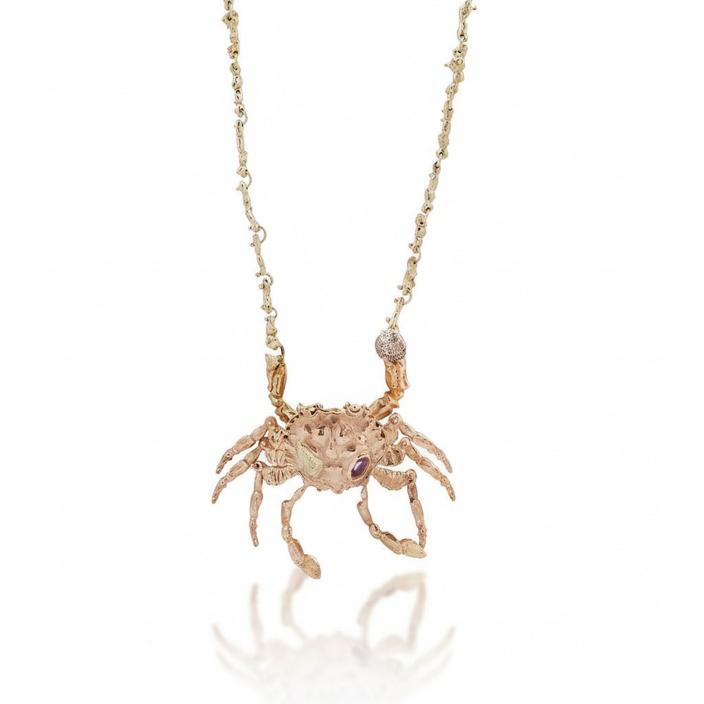 Hand-carved kinetic crab locket by Alexis Pavlantos in recycled 14k rose gold, featuring articulated legs, ruby accents, and a handmade 14k yellow gold coral-inspired chain.