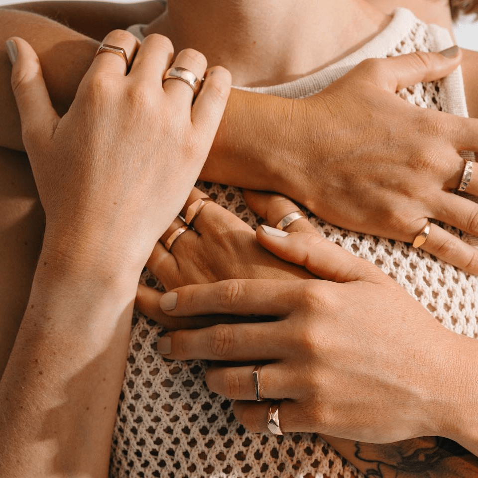 Stacked gold rings shown on intertwined hands in a warm lifestyle portrait.