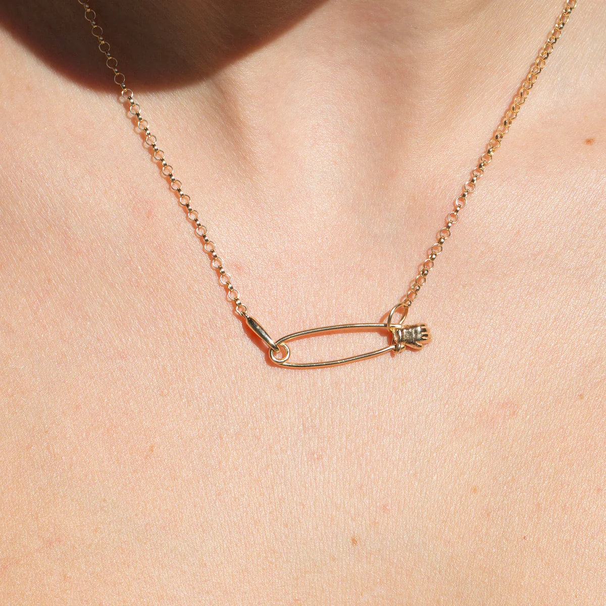 Close-up of the 14k gold hand safety pin charm worn on the neck.