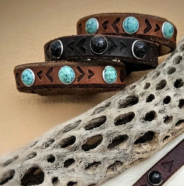 Close-up of Kelly Horrigan leather cuff bracelets showing natural turquoise cabochons, textured brown leather, and sterling silver bezel settings.