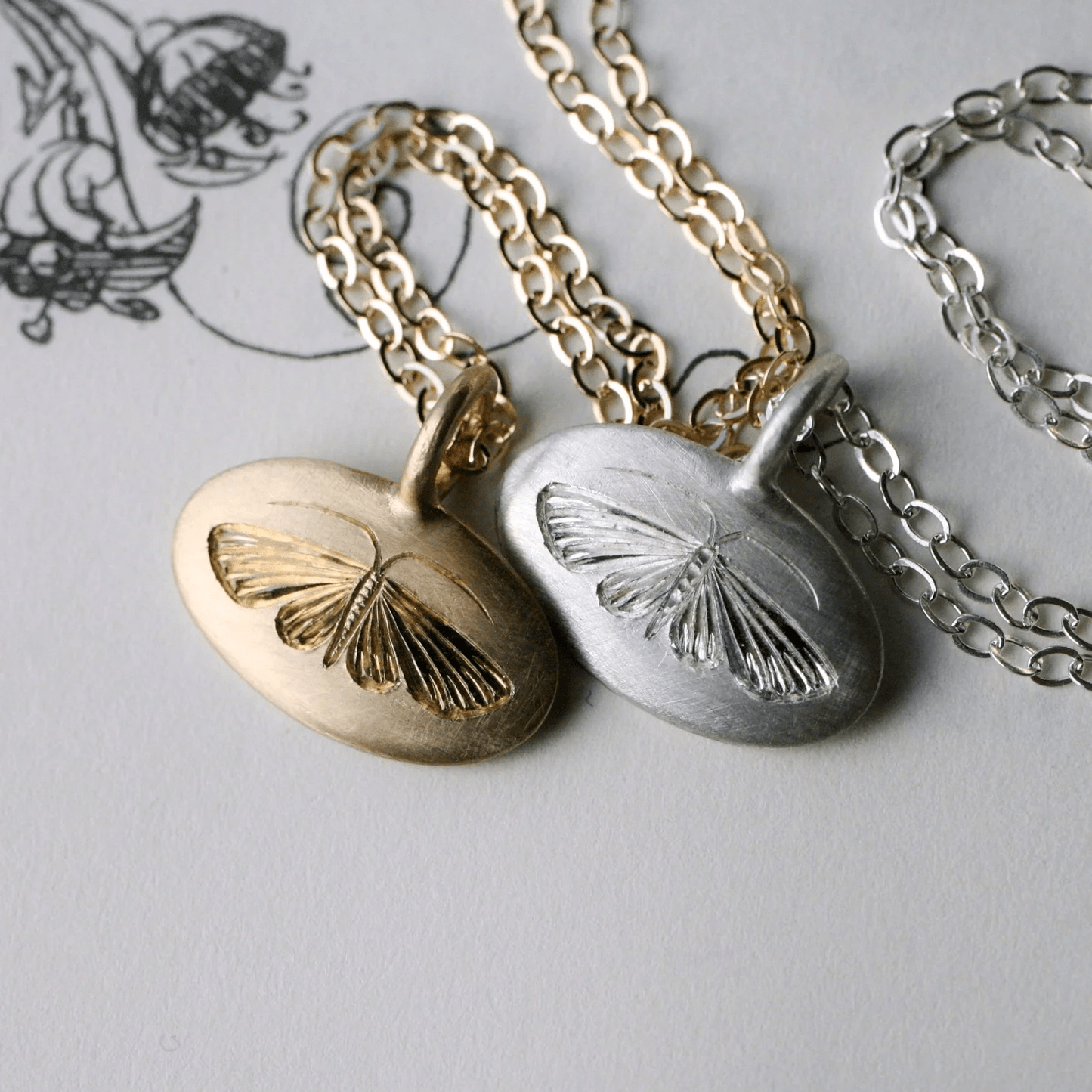 Gold and sterling silver hand-engraved house moth pendants displayed together on chains.