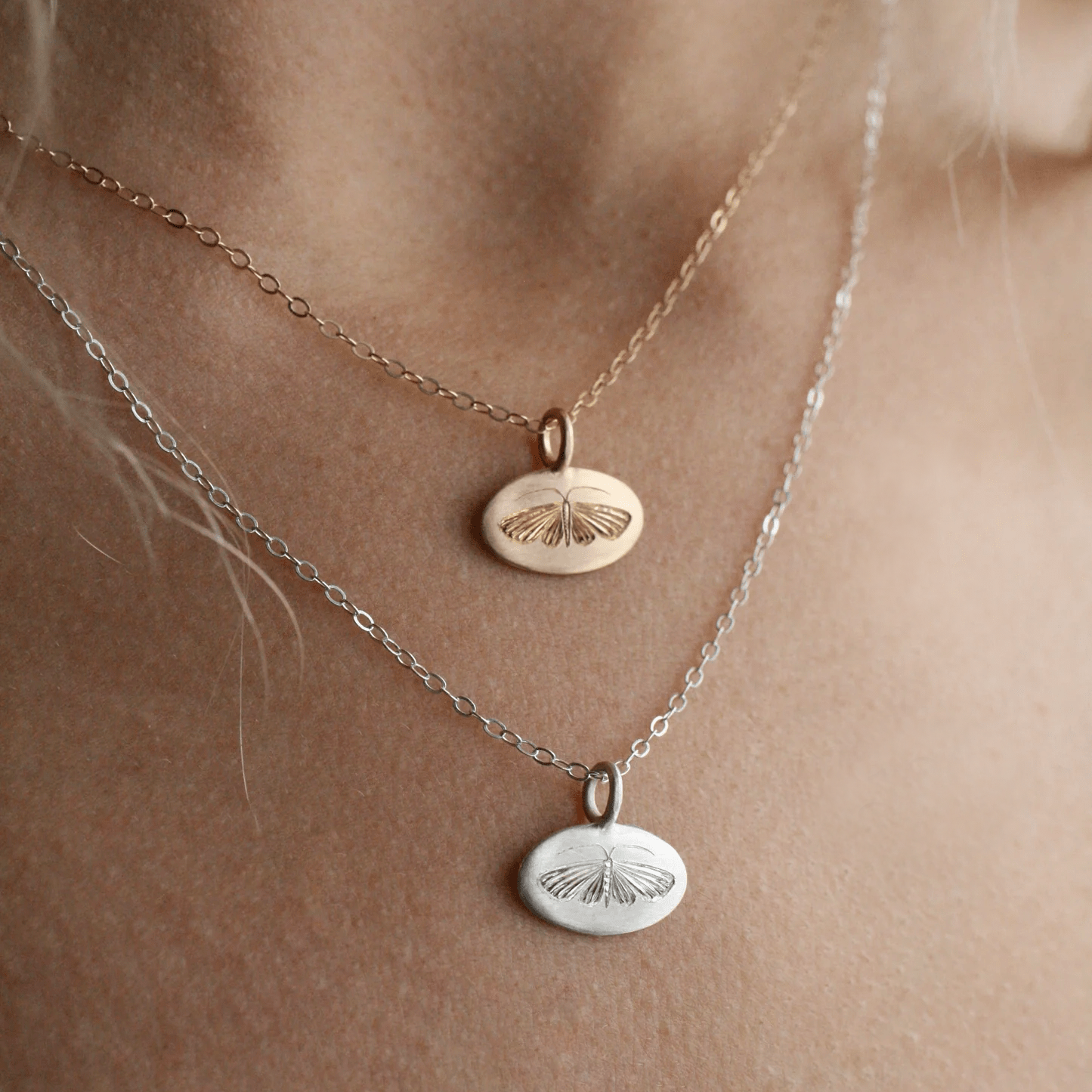 Gold and sterling silver house moth pendants worn layered on the neck.