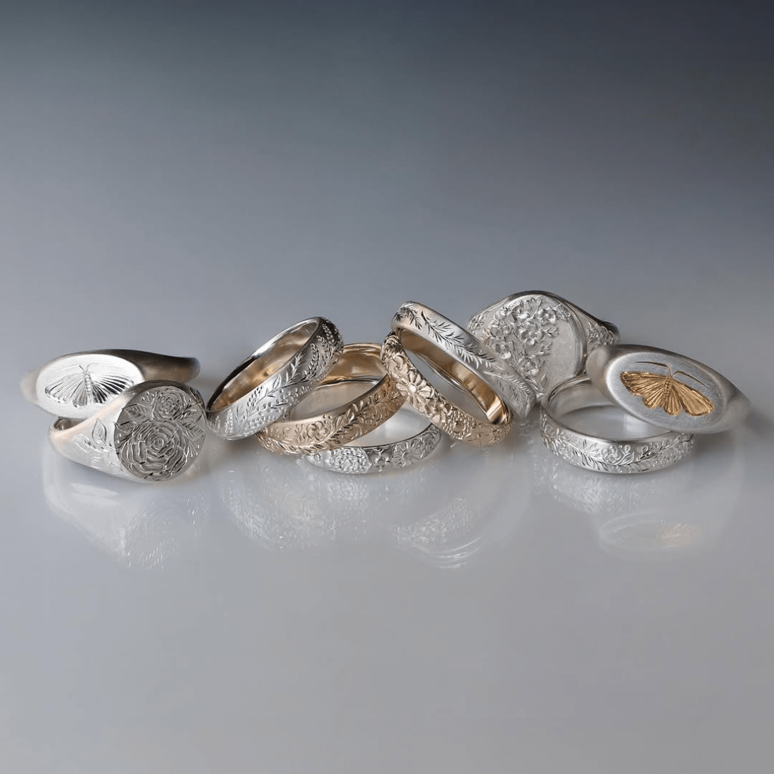 A mixed group of house moth rings in gold, silver, and two-tone designs arranged on a reflective surface.