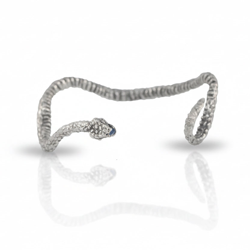 Hand-carved Ichos Snake Cuff by Alexis Pavlantos in sterling silver, featuring a sculptural coiled snake design with a blue sapphire set in its mouth.