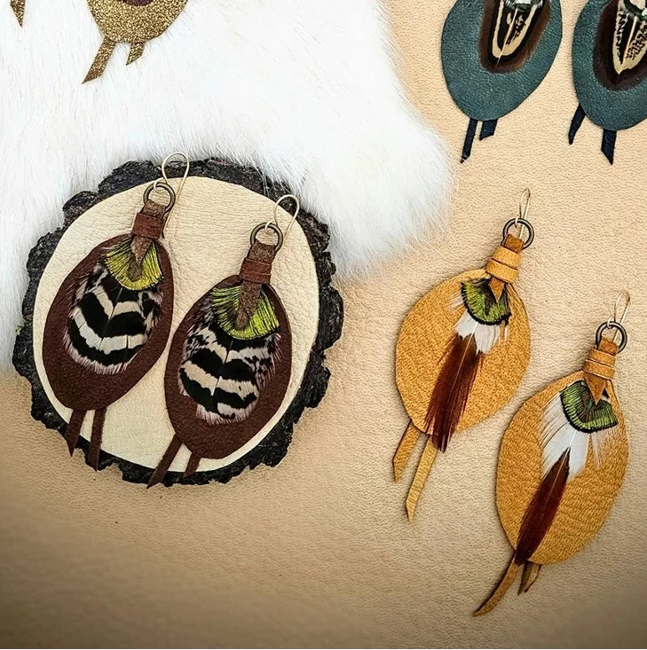 Collection of Kelly Horrigan handmade leather and feather earrings in russet brown, emerald green, cream, and golden yellow with natural patterned feathers.