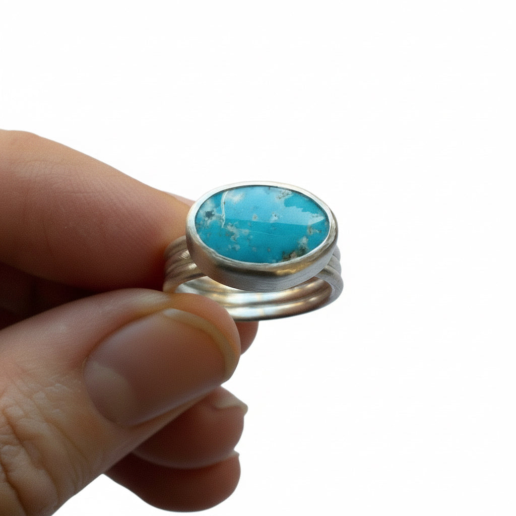 Turquoise stone ring with silver band held by a hand against a white background