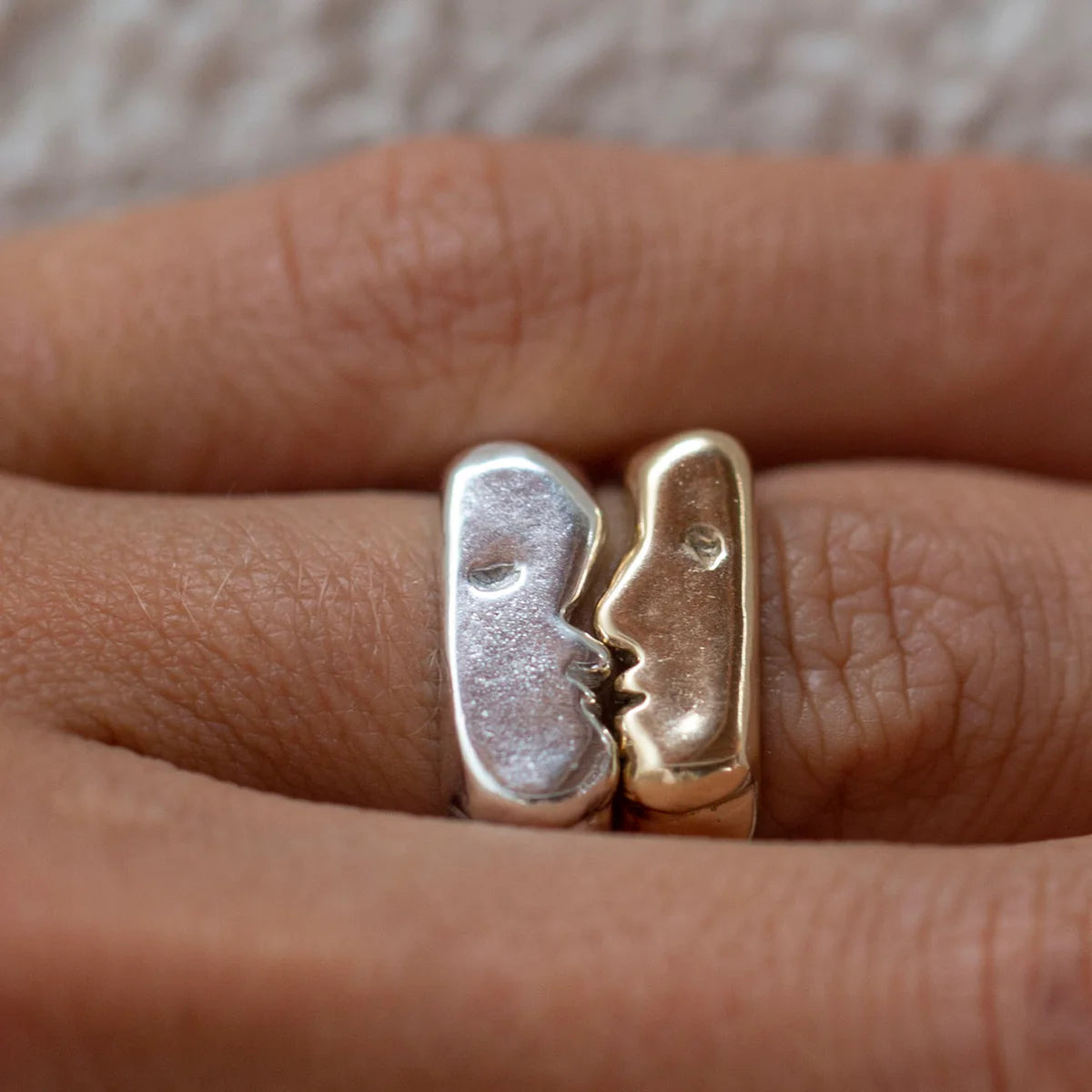 Close-up of kissing signet rings worn on a hand, highlighting the sculpted kiss detail.