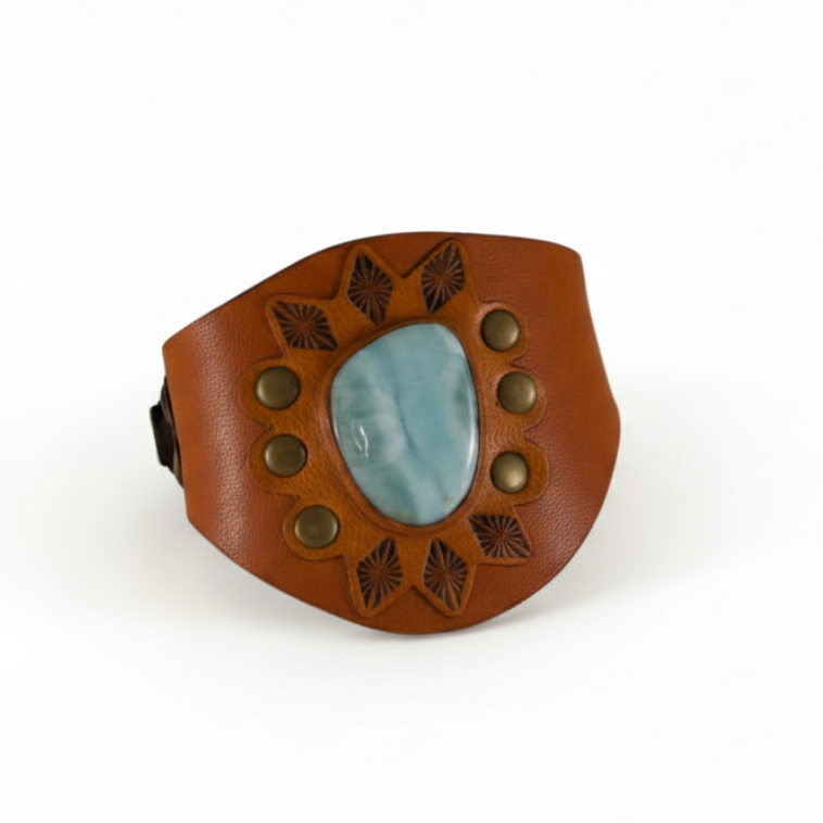 Handmade Larimar leather cuff bracelet by Kelly Horrigan featuring a natural pale blue Larimar stone, warm brown hand-tooled leather, decorative metal studs, and geometric detailing.