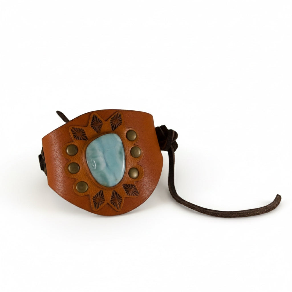 Front view of a Kelly Horrigan Larimar cuff bracelet showing a blue gemstone surrounded by decorative metal studs and hand-tooled geometric patterns on brown leather.