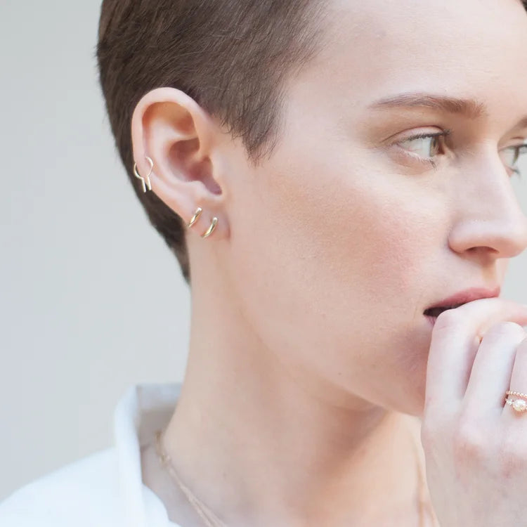 Woman wearing a 14k gold Loopdie minimalist single earring, shown in a close-up portrait.