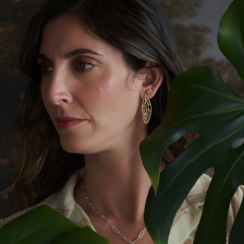 Model wearing sculptural gold cicada wing earrings by Alexis Pavlantos, showing their delicate openwork design and length against the ear.