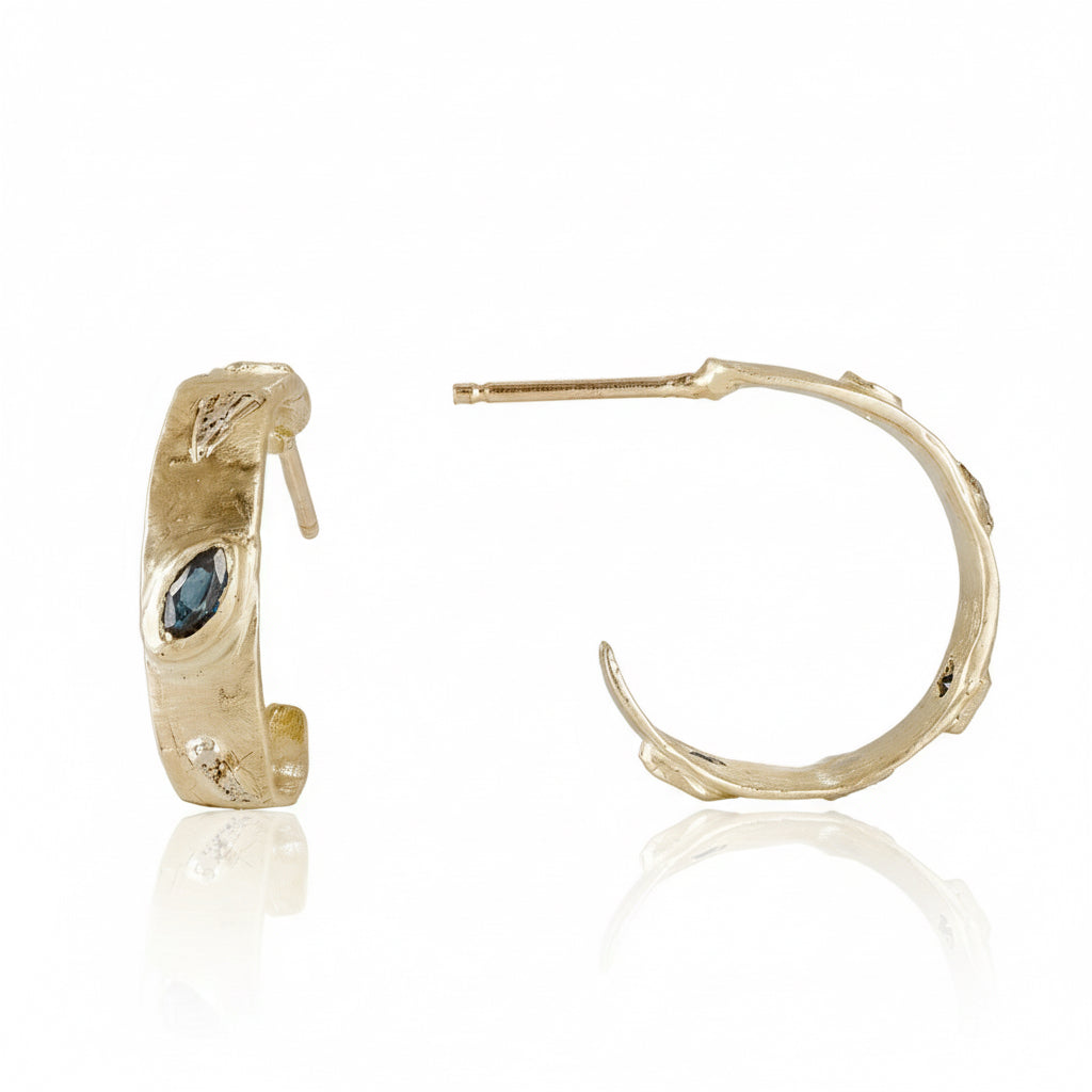 Front and side views of handcrafted Meta Hoop Earrings by Alexis Pavlantos in 14k yellow gold with rose gold accents, featuring blue sapphires, organic sculptural texture, and an open hoop design.