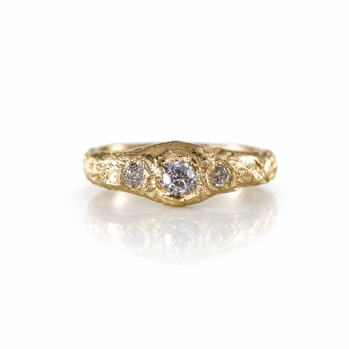 Detailed view of three old mine cut diamonds in integrated gold settings, surrounded by hand-carved geological texture in solid 14k yellow gold.