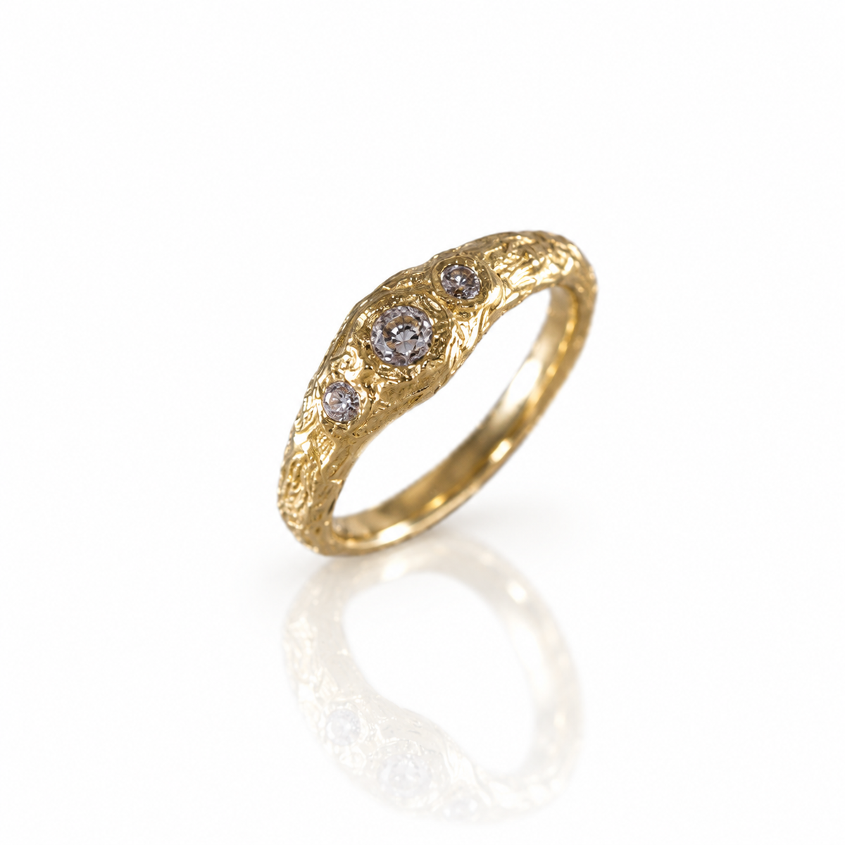 Angled view of a sculptural 14k yellow gold ring with three old mine cut diamonds nestled into an organic, rock-textured band by Alexis Pavlantos.