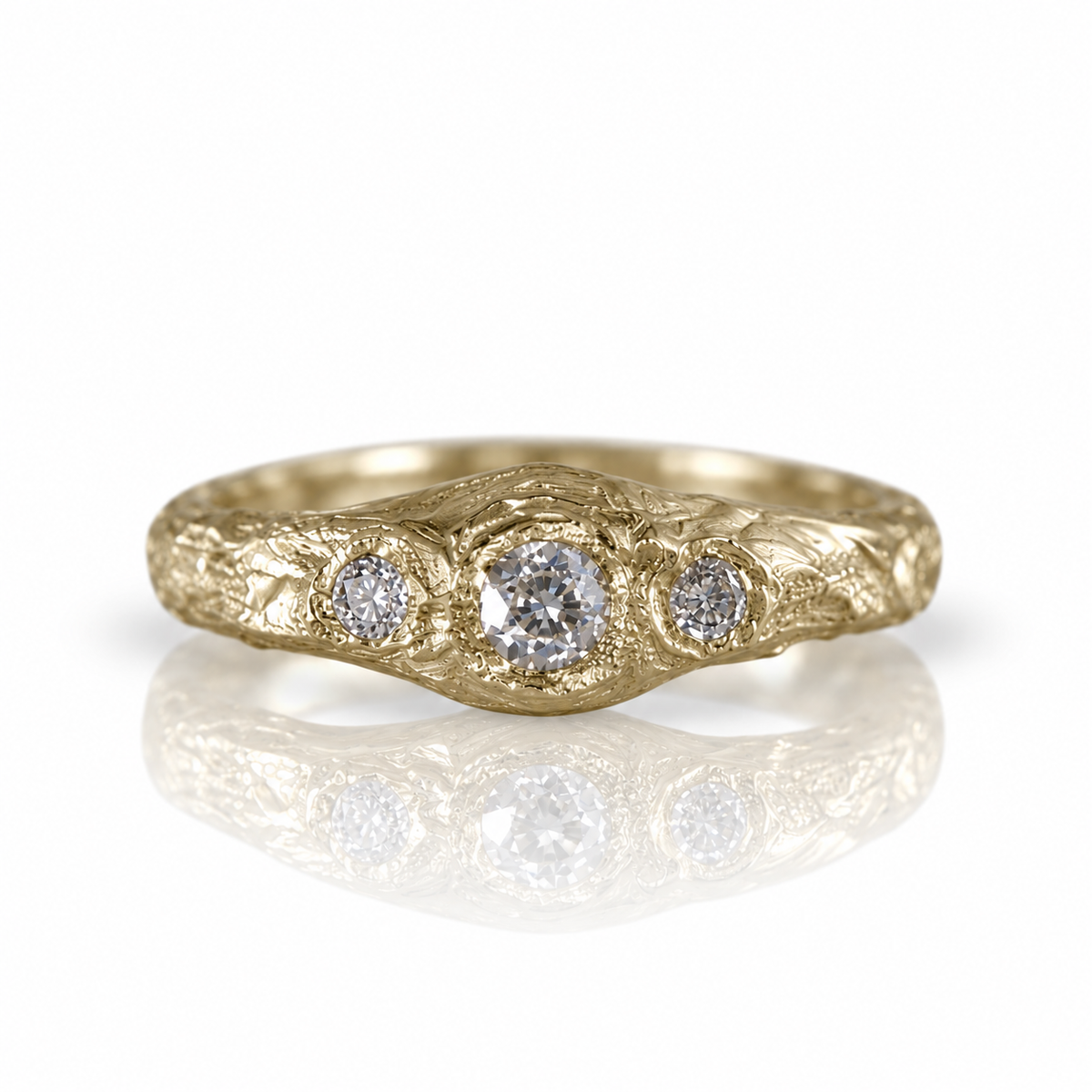 Close-up of a handcrafted 14k yellow gold three-stone diamond ring featuring antique-style old mine cut diamonds and a substantial sculptural band.