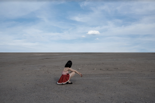 Cloud by Nicole Cudzilo, an archival pigment photography print showing a lone figure in red beneath a vast blue sky on a minimalist desert landscape.