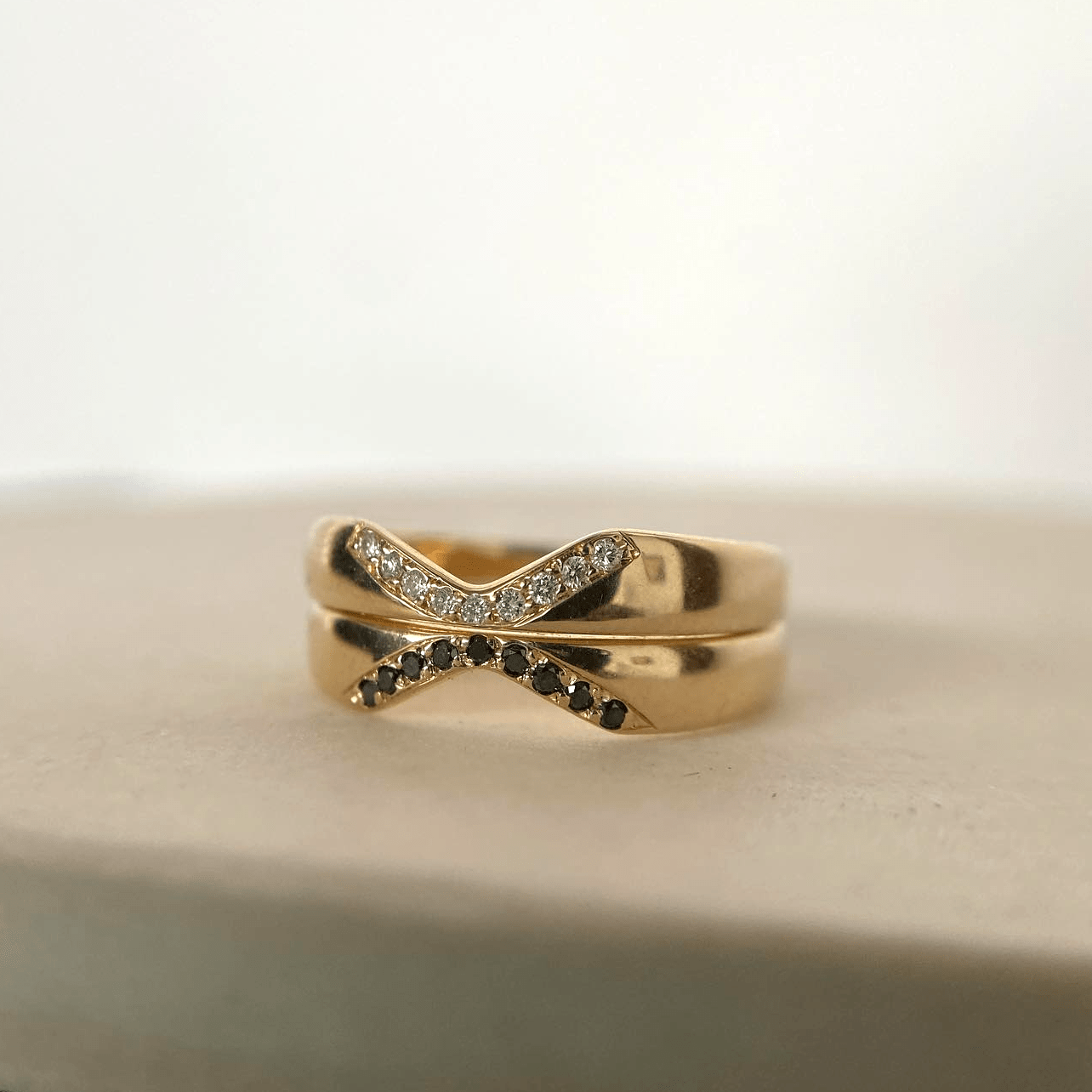 A 14k yellow gold Notch Halo Ring stacked with a black-diamond version, displayed on a soft white surface.
