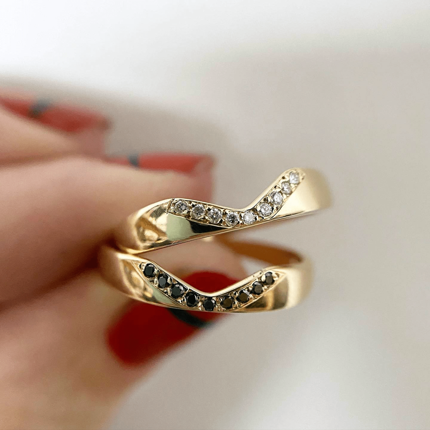 Hand holding a 14k yellow gold Notch Halo Ring, showing both the white and black diamond versions.