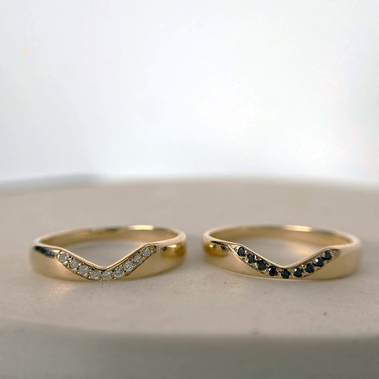 Two 14k yellow gold Notch Halo Rings on a white background, one set with white diamonds and one with black diamonds.